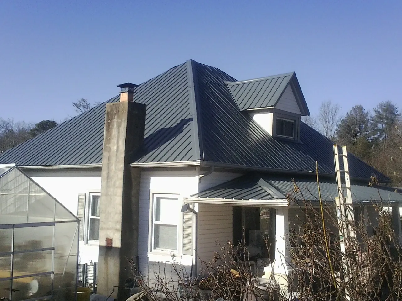 Dark blue standing seam metal roof on a white farmhouse with dormer — Slate & Tile Roof Repair by Roofing Brothers in Collinston