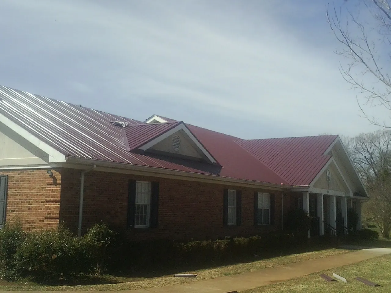 Red metal roof with gabled entries on a long brick building, from a Hail Damage Roof Repair job in Collinston