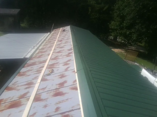 Old rusted panels beside newly installed green metal roofing — Wind Damage Roof Repair by Roofing Brothers in Collinston