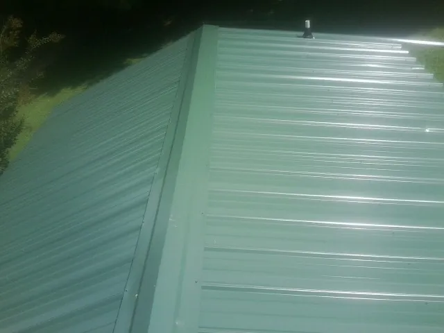 New green metal panels meeting at the ridge of a roof — Flat Roof Repair work by our crew in Collinston
