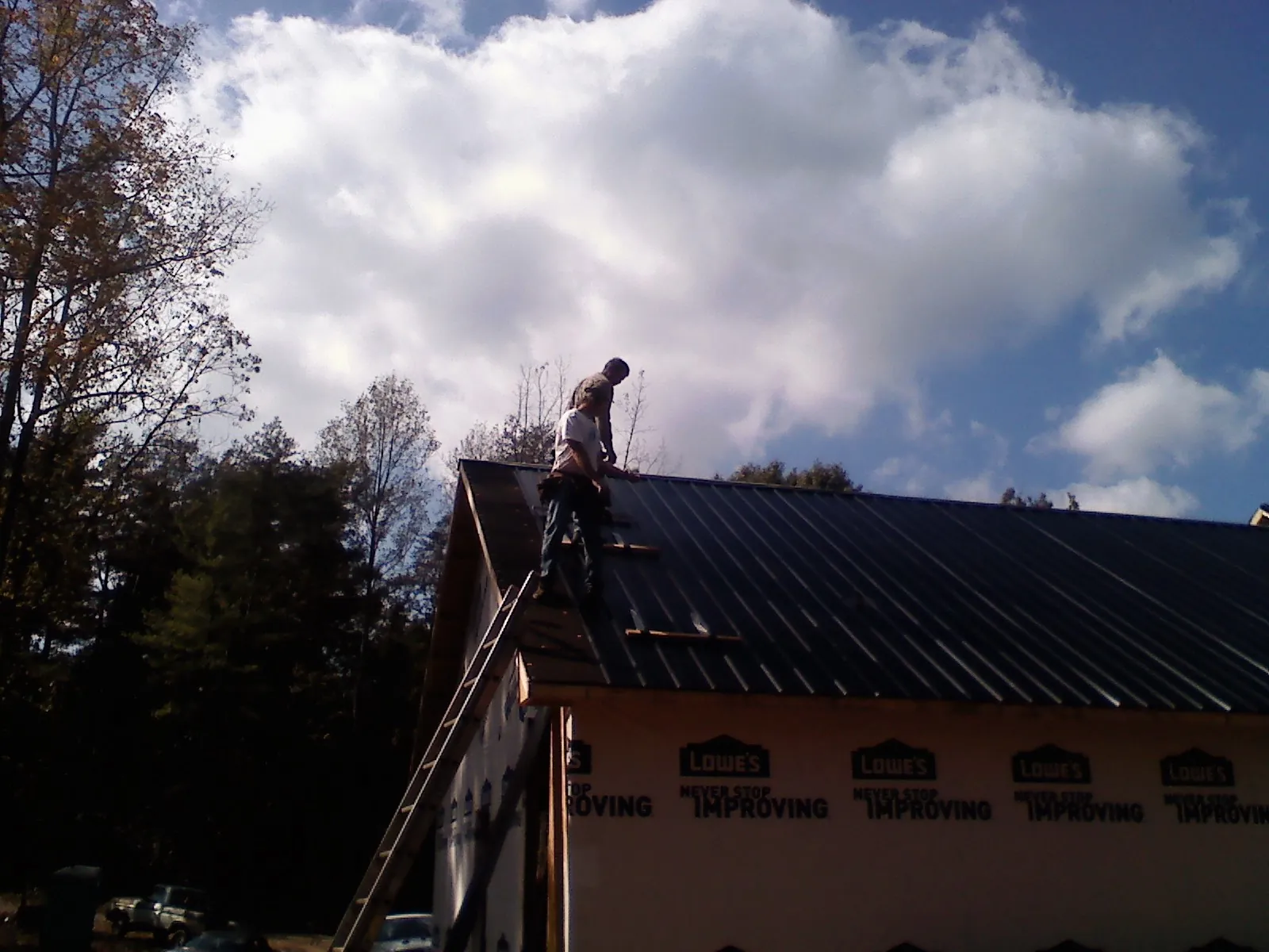 Roofer fastening dark metal panels high against a cloudy sky, from a Roof Inspection job in Collinston