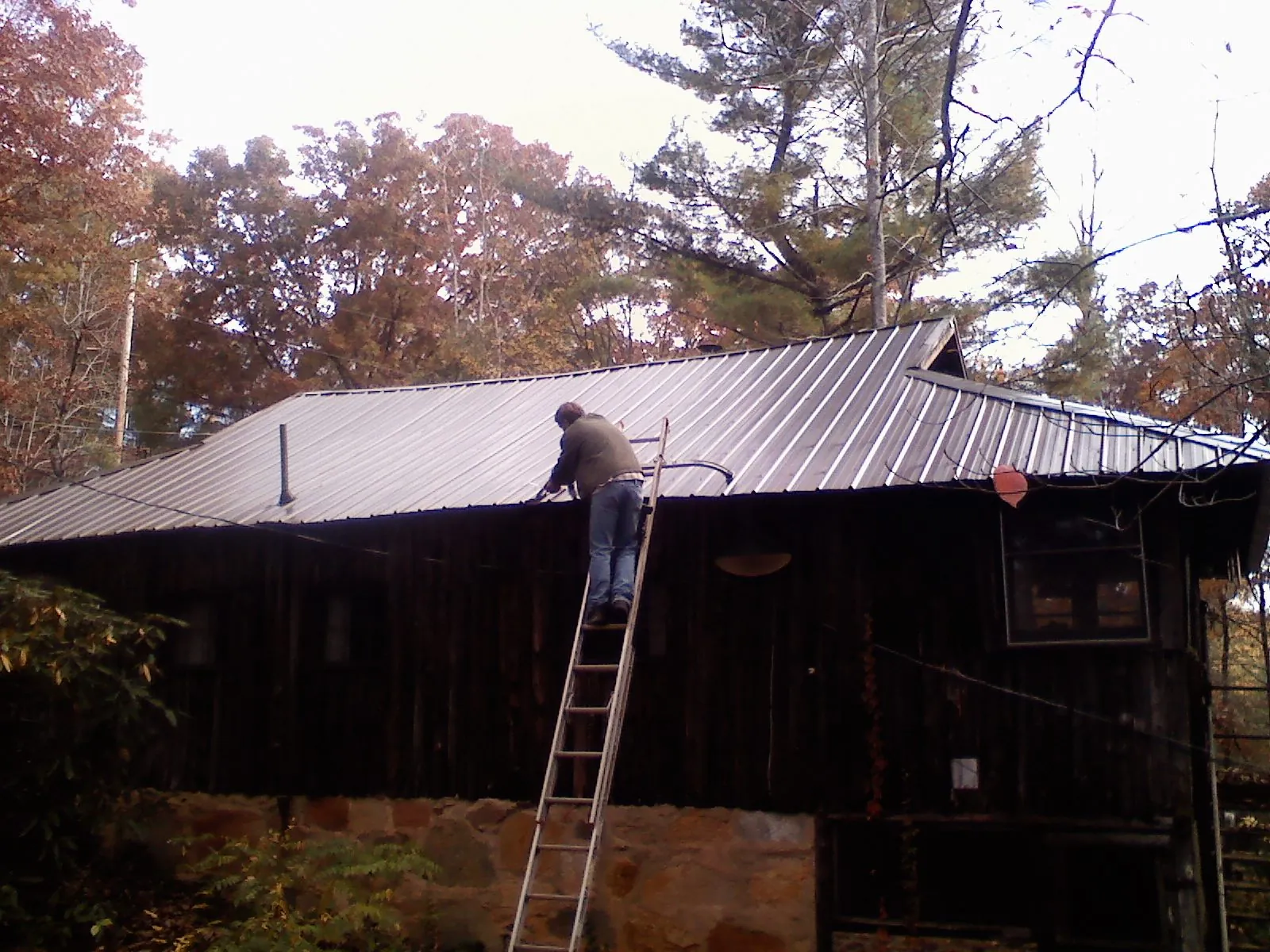 Roofer on a ladder working along the edge of a cabin metal roof in Collinston