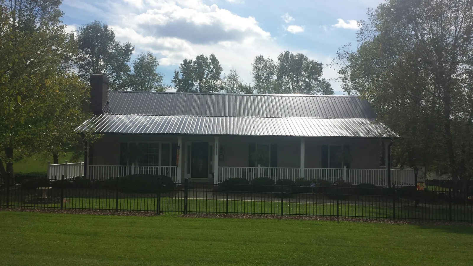Gray metal roof on a brick ranch with a full width front porch — Gutter Guard Installation work by our crew in Collinston