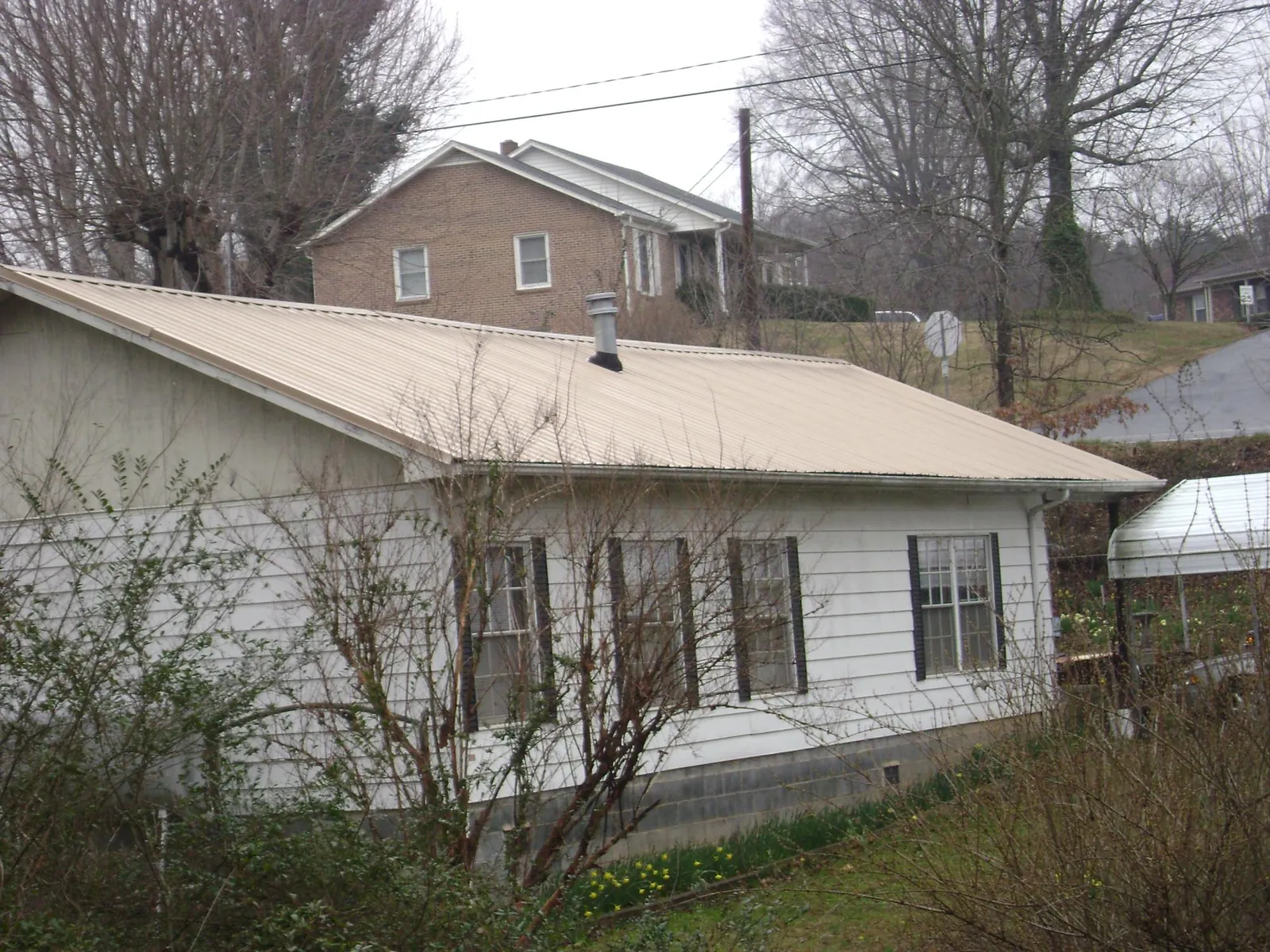 Tan metal roof on a white sided house set into a hillside — Commercial Roofing by Roofing Brothers in Collinston