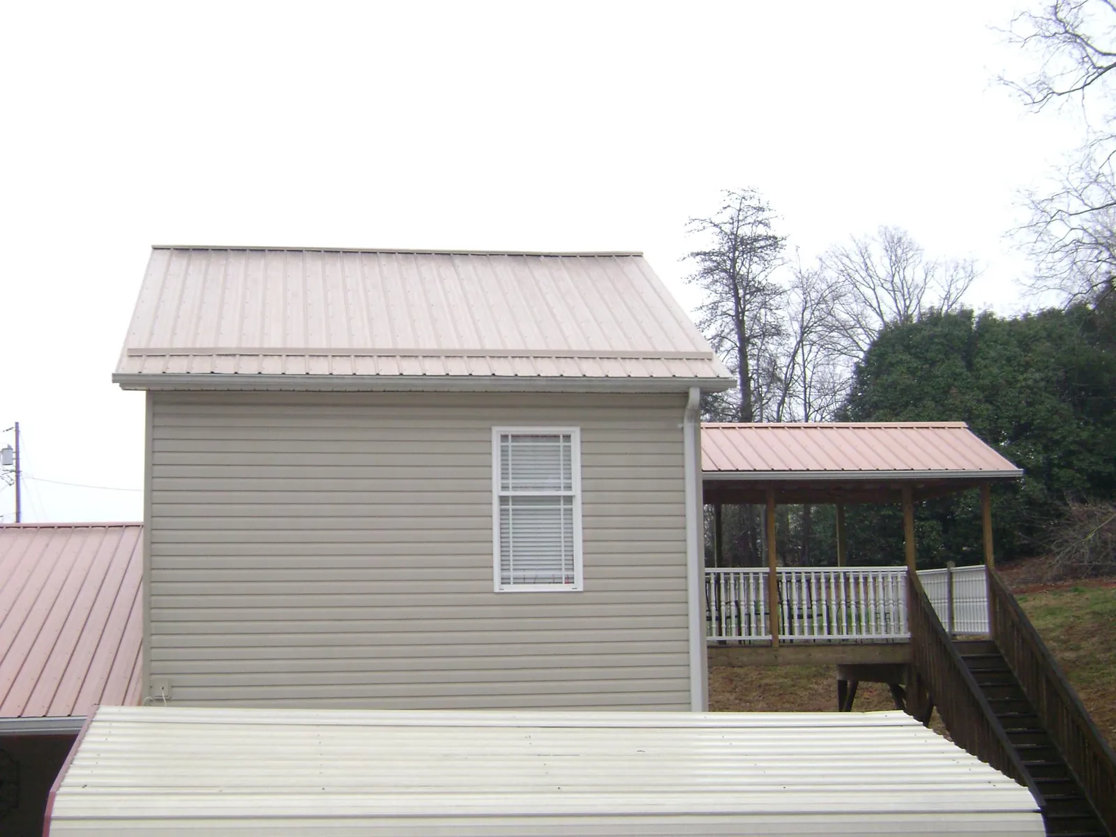 Tan metal roofs on a two story addition and attached porch, from a Roof Replacement job in Collinston